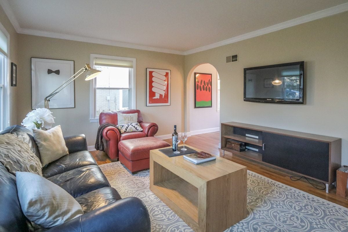 Living room with black leather sofa, red armchair, patterned rug, and wall-mounted television.
