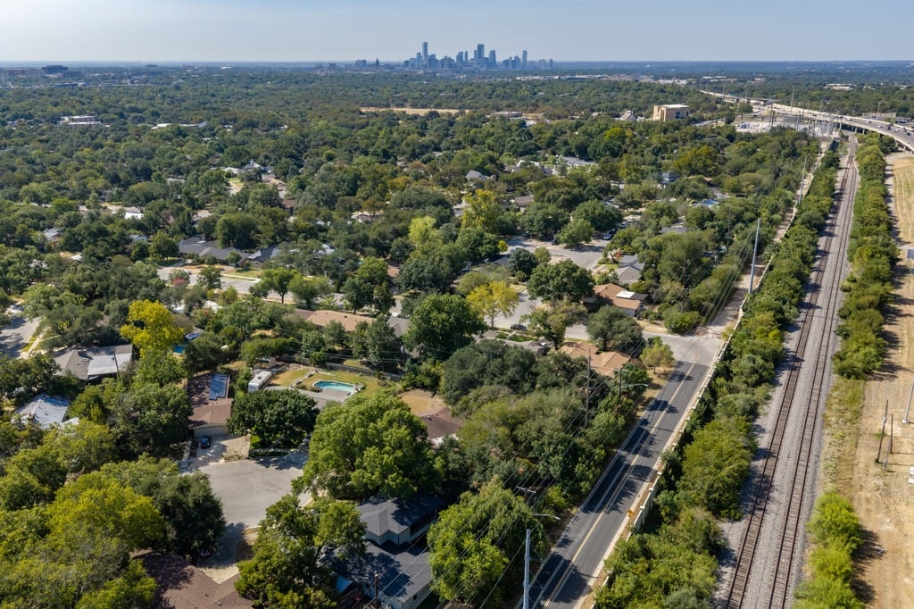 Leafy neighborhood, rail tracks, and downtown Austin skyline seen from above.