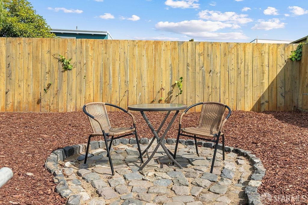 Backyard patio with two woven chairs and a round table on circular stone paving.