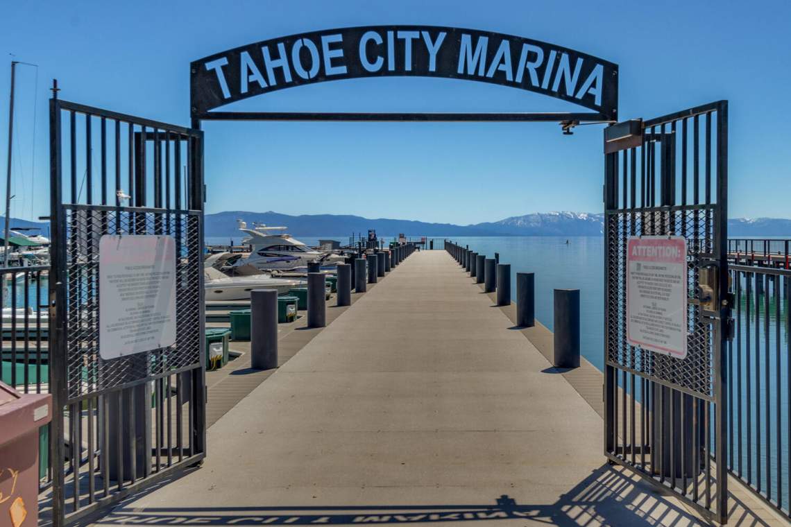Tahoe City Marina entrance frames a dock extending onto Lake Tahoe, with boats and mountains beyond.