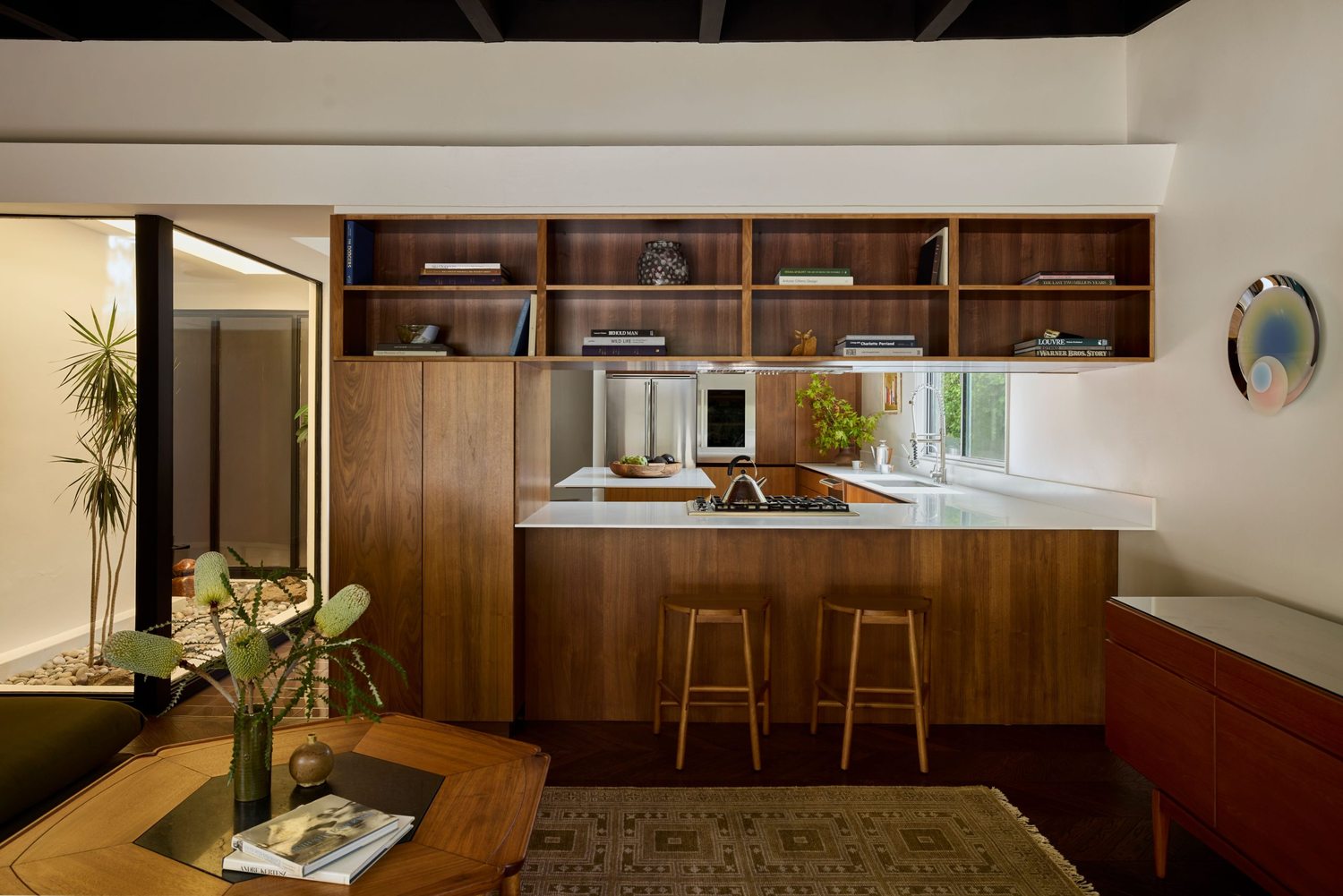 Kitchen with walnut millwork, integrated shelving, and a view through to a breakfast bar with rattan stools.