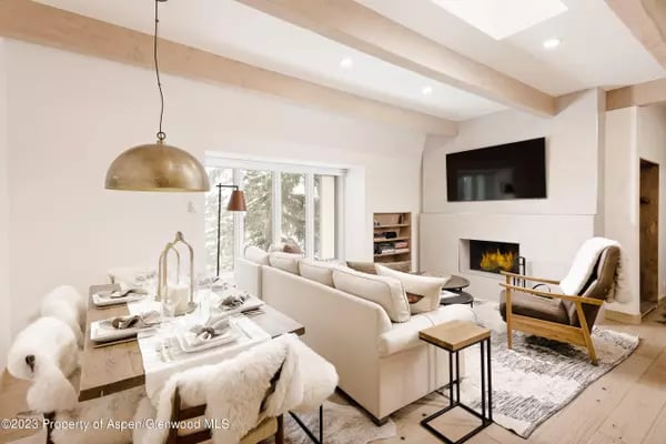 Open-plan living and dining room with exposed ceiling beams, a white sectional, and a fireplace.