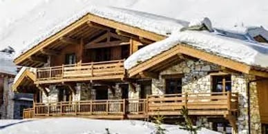 Snow-covered chalet with timber balconies and a stone facade.