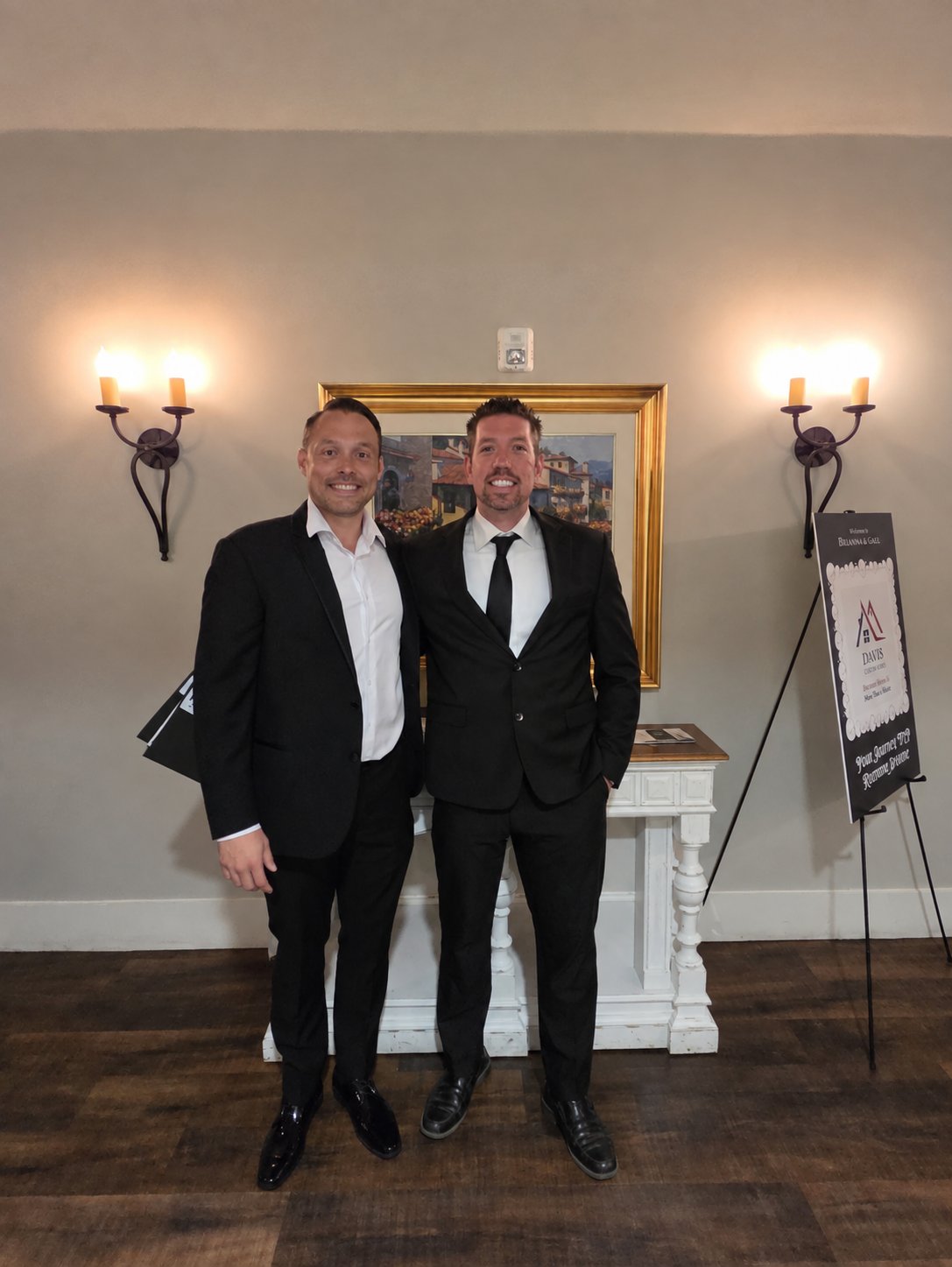 Two men in dark suits pose beside a freestanding Davis sign.