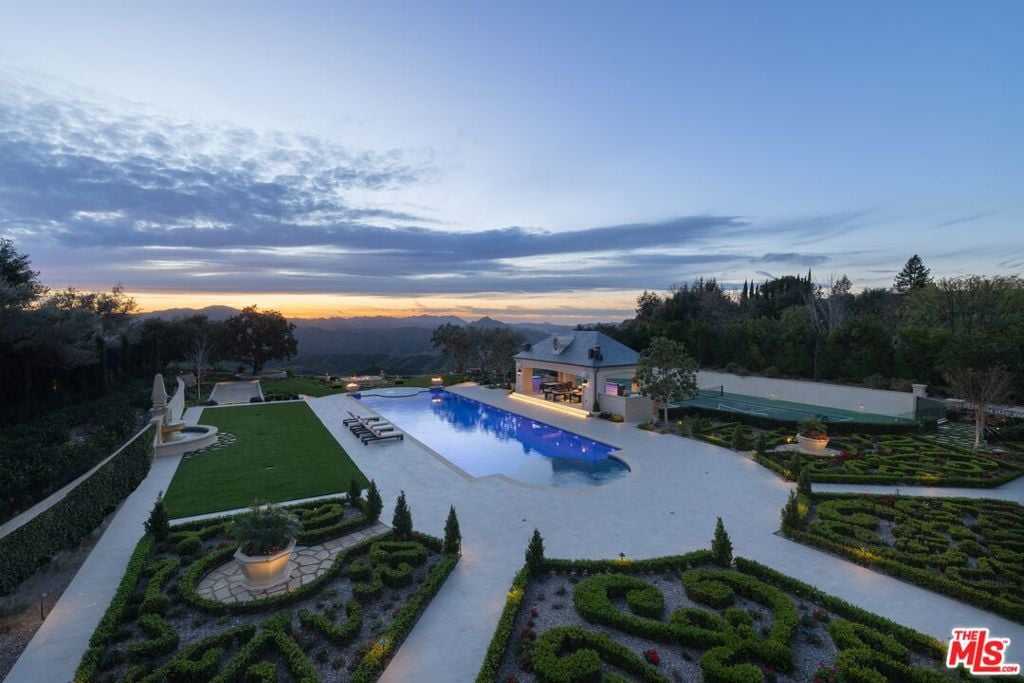 Estate backyard with a blue swimming pool, formal gardens, and mountain views at dusk.