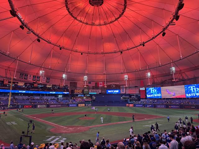 Baseball field beneath Tropicana Field’s red-lit dome, with a “RAYS WIN!” display.