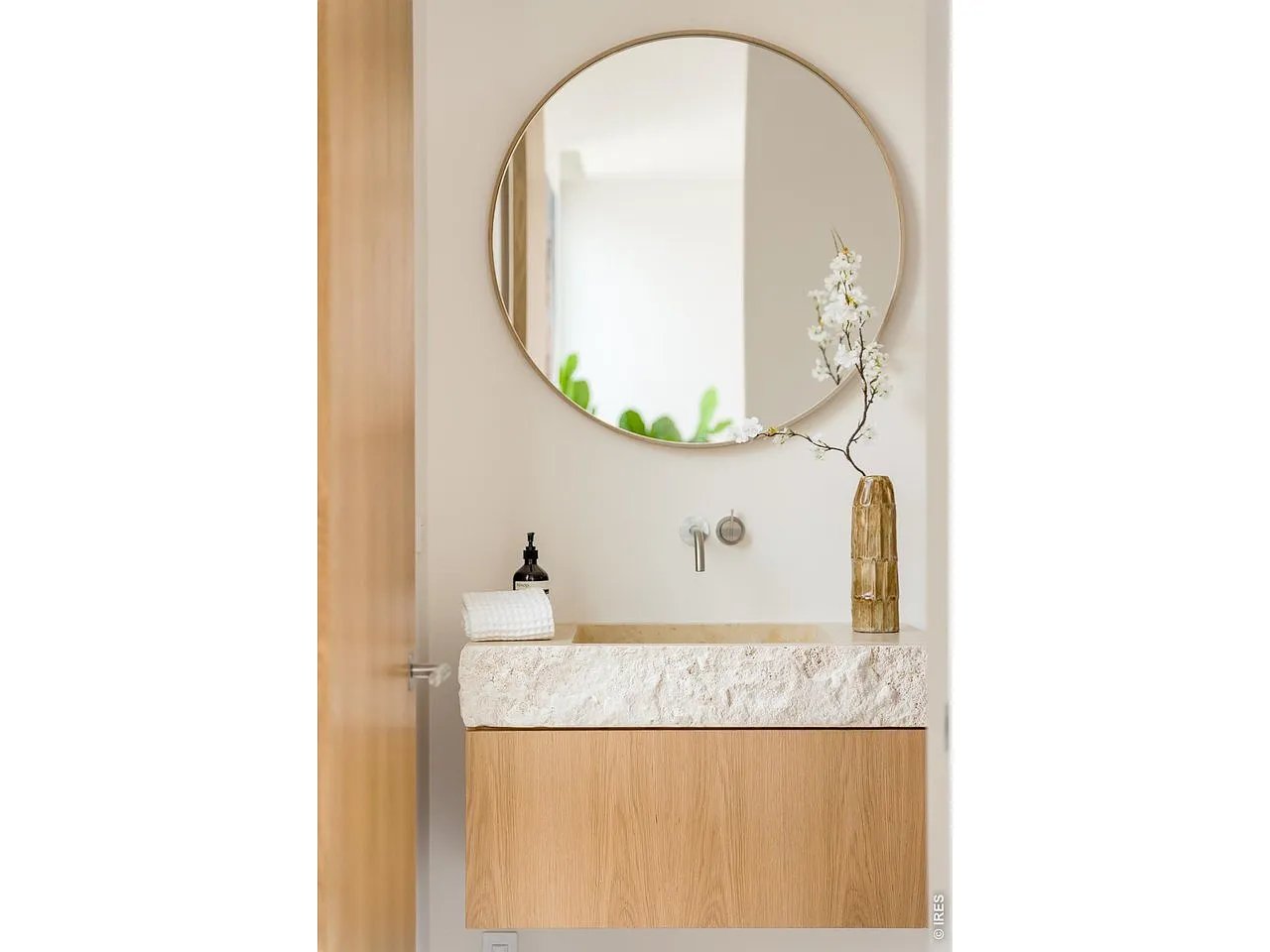 Bathroom vanity with a textured stone basin, light wood cabinet, and round mirror.