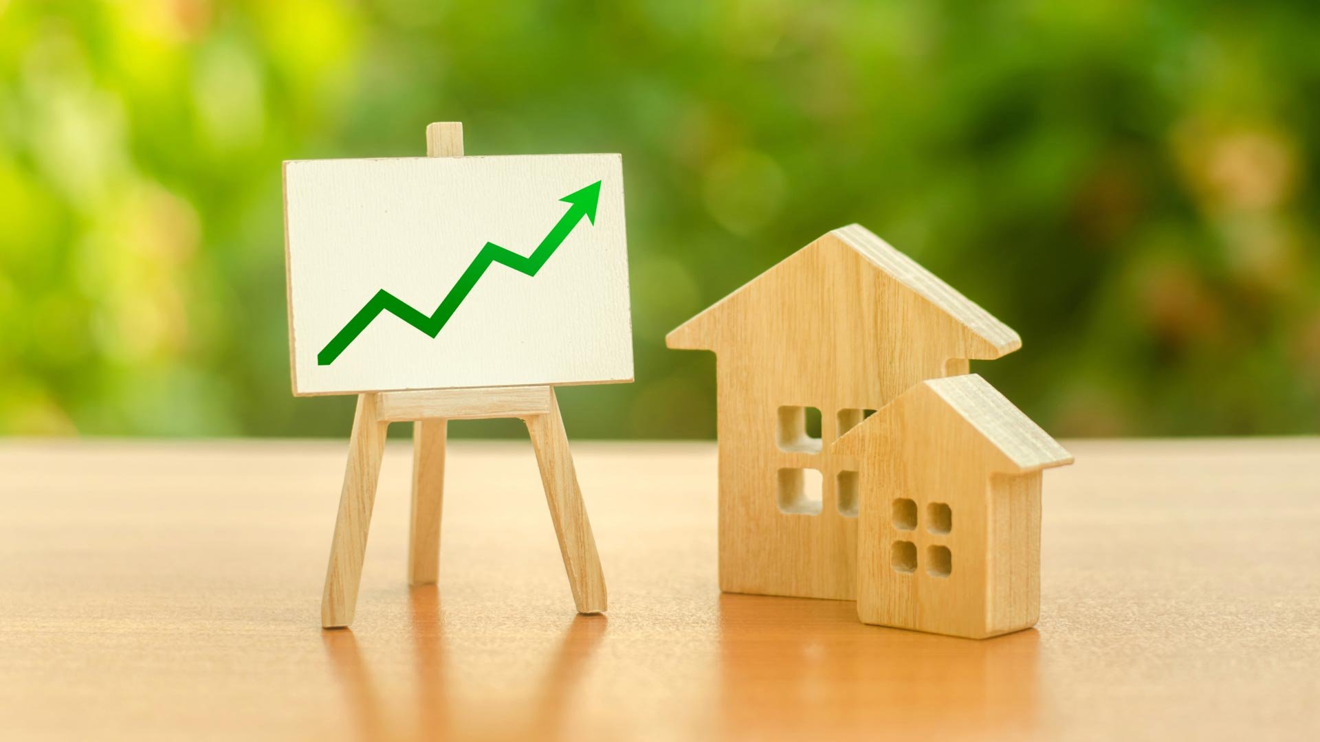A descriptive close up of small wooden house models sitting next to a miniature easel displaying a sharp green upward trending arrow graph, illustrating the data driven real estate pricing strategy required when navigating a shifting property landscape and deciding how to price your home to secure maximum competitive engagement when selling a home GTA families value.