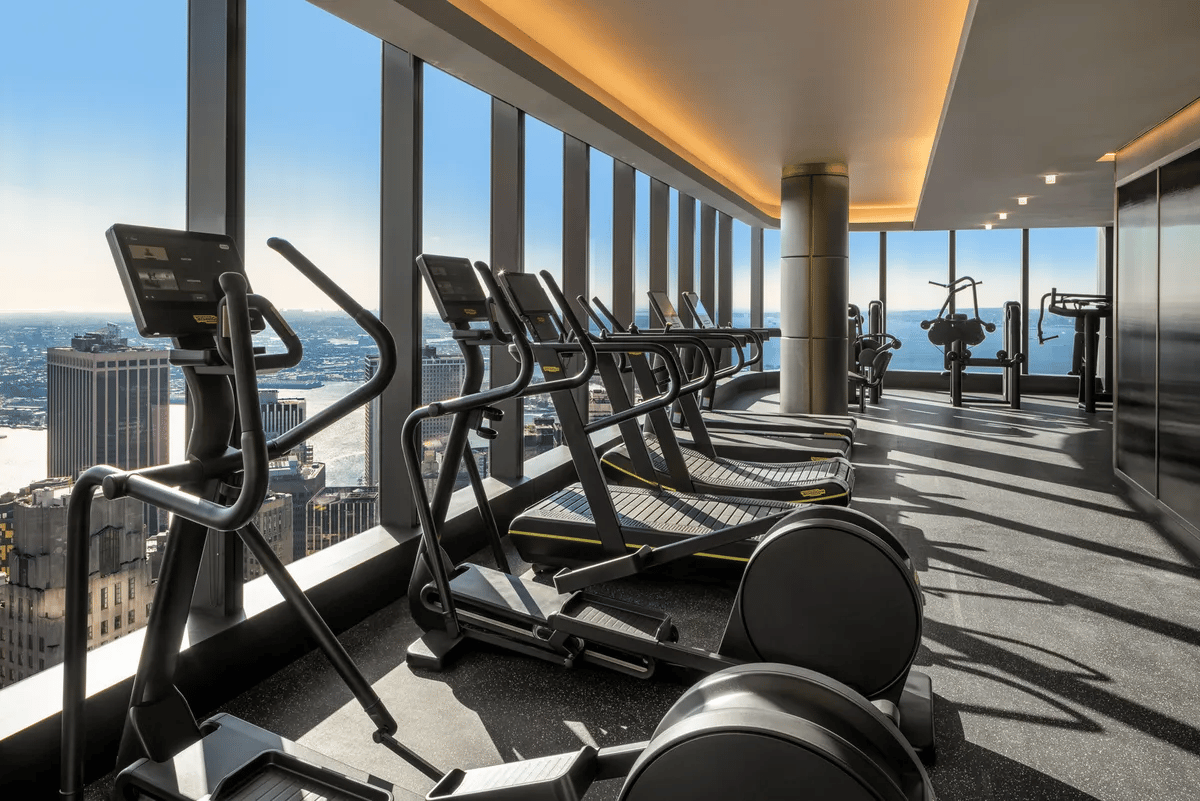 High-rise fitness center with cardio equipment and floor-to-ceiling windows overlooking the city and water.