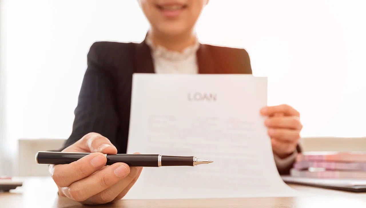 A woman holds a loan document and offers a pen.