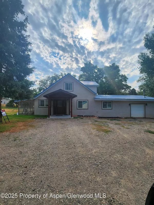 Gray house with a peaked entry and attached garage beyond a wide gravel driveway.