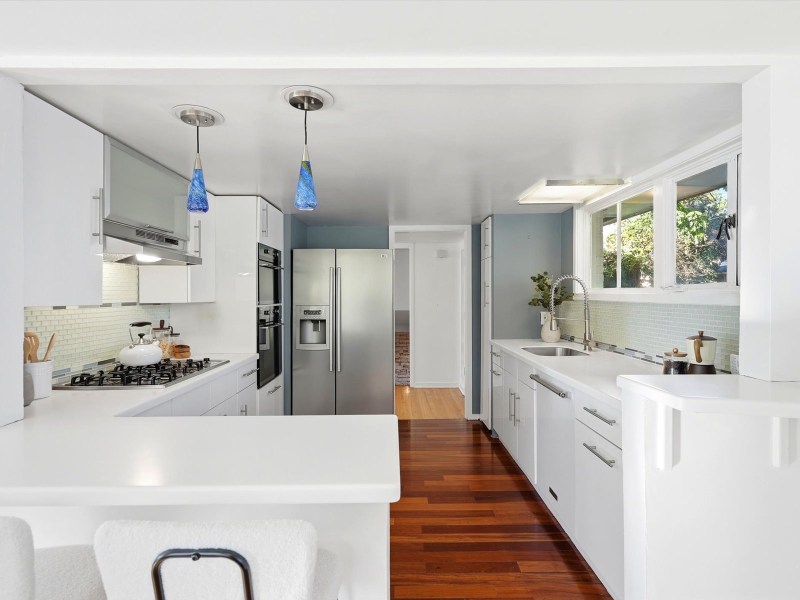 Modern kitchen with white cabinetry, stainless steel appliances, blue tile backsplash, and dark wood floors.