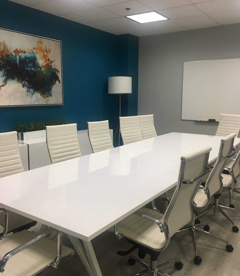 Conference room with a long white table, white chairs, abstract wall art, and a wall-mounted whiteboard.