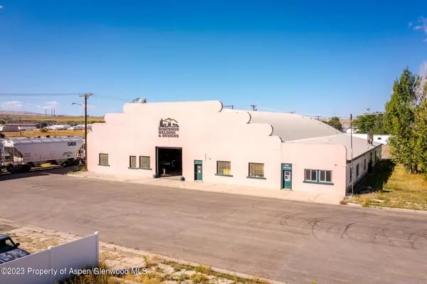 Pale stucco commercial building with a stepped parapet and broad paved parking area.