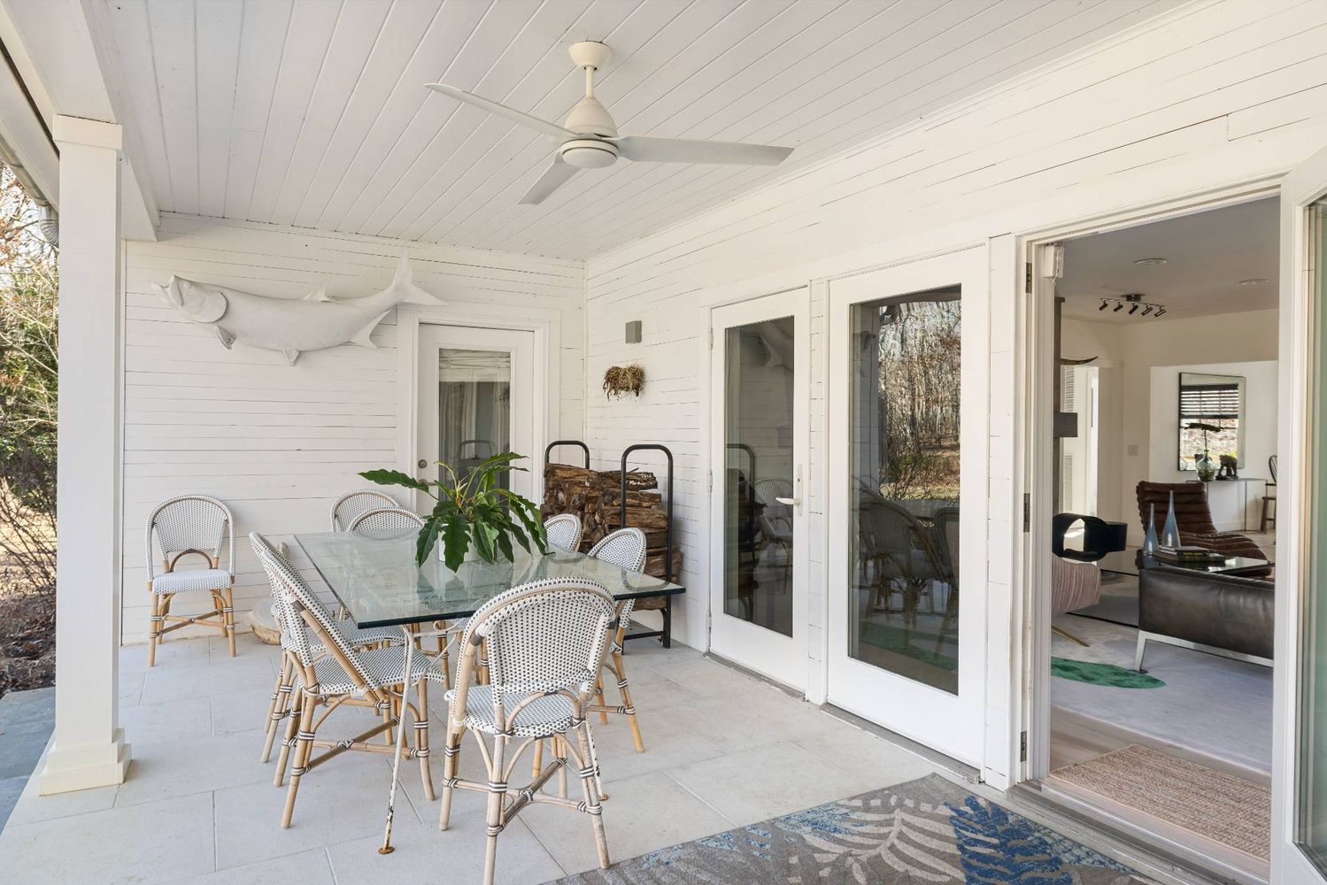 Covered patio with a glass dining table, woven chairs, and doors opening into the living room.