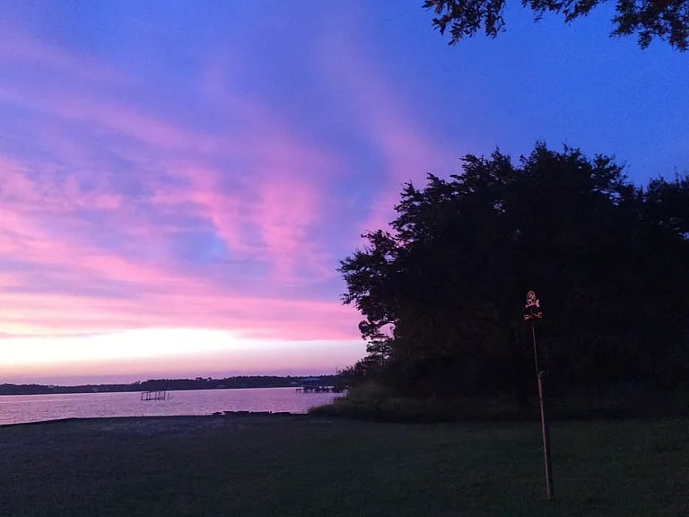 Lake at dusk beneath pink and purple clouds, with trees along the shoreline.
