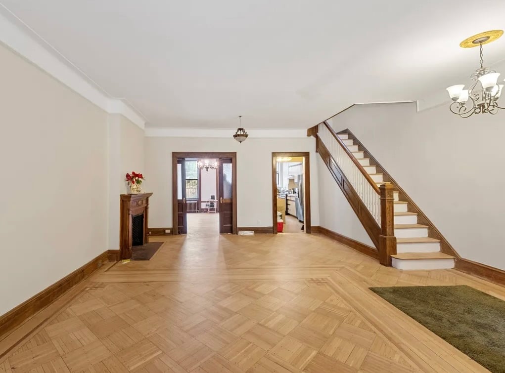 Spacious brownstone interior in Brooklyn featuring hardwood floors, decorative fireplace, and classic wood staircase.