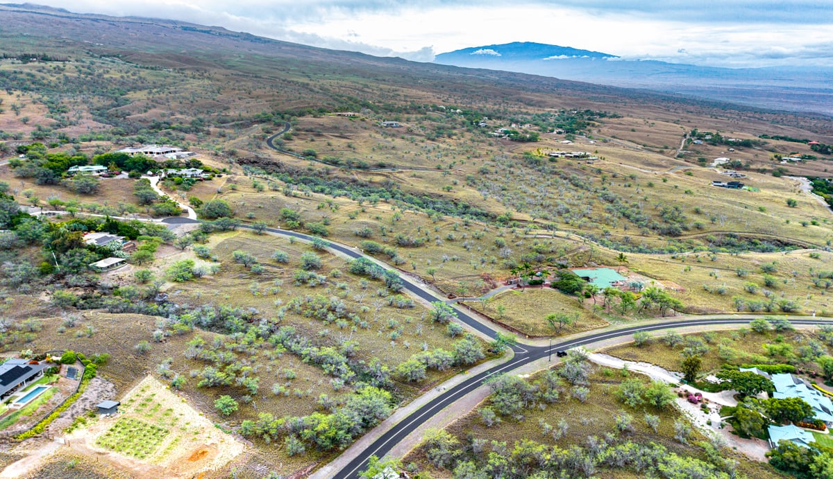 Aerial view of a vacant parcel amid homes, winding roads, and rolling hills.