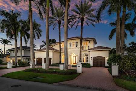 Two-story stucco home with arched windows and a curved driveway beneath tall palm trees at dusk.
