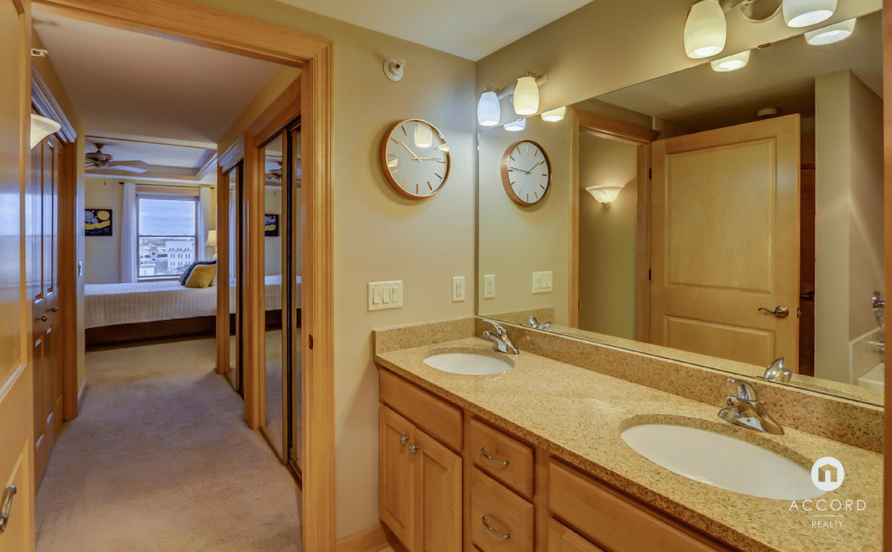 Condo bathroom with a double-sink granite vanity, opening to a bedroom with a city view.