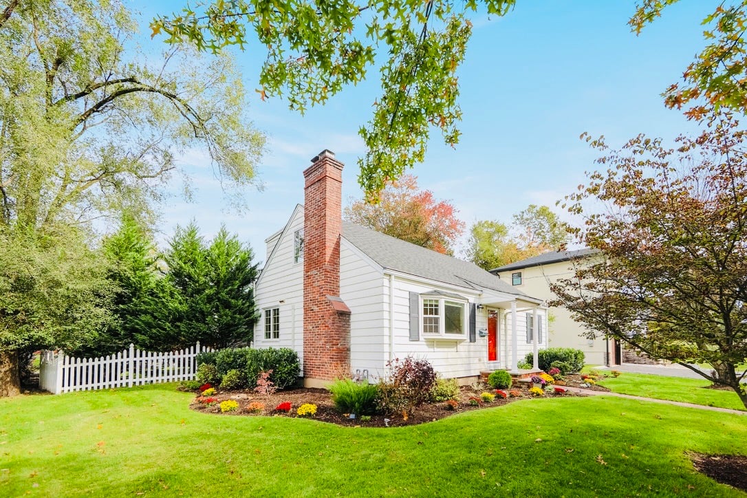 A charming white home with a red door and brick chimney on County Road in Demarest, NJ, featuring a manicured front lawn.