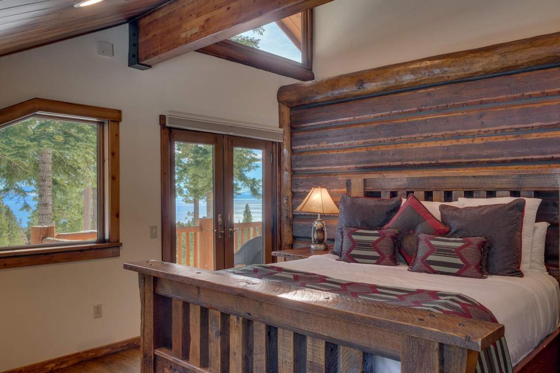 Rustic log-cabin bedroom with a timber bed and lake views through glass doors.
