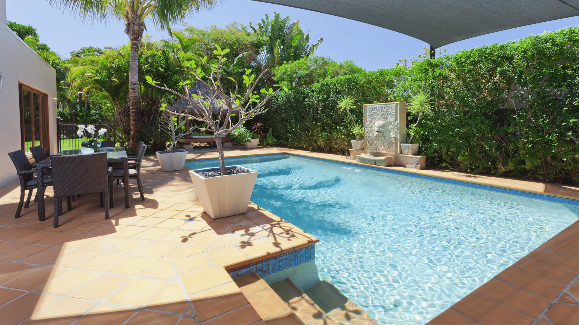 Backyard swimming pool with tropical landscaping, a stone fountain, and covered outdoor dining area.