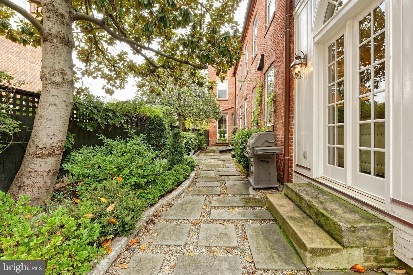 Brick home courtyard with a stone walkway, leafy garden, and French doors.