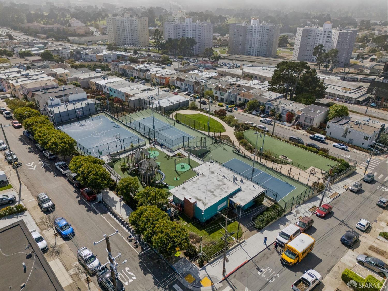 Aerial view of a neighborhood property beside fenced basketball and tennis courts and a playground.