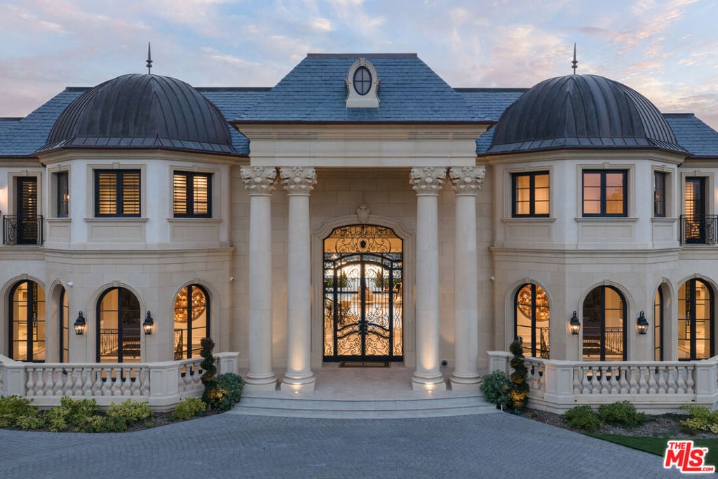 Mansion entrance with twin domed towers, tall columns, and an ornate iron gate at dusk.