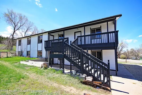 White two-story home with a black-railed deck and long staircase overlooking the lawn.