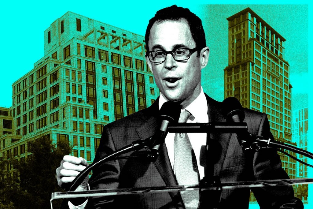 Man in glasses speaking at a lectern with city high-rises behind him.