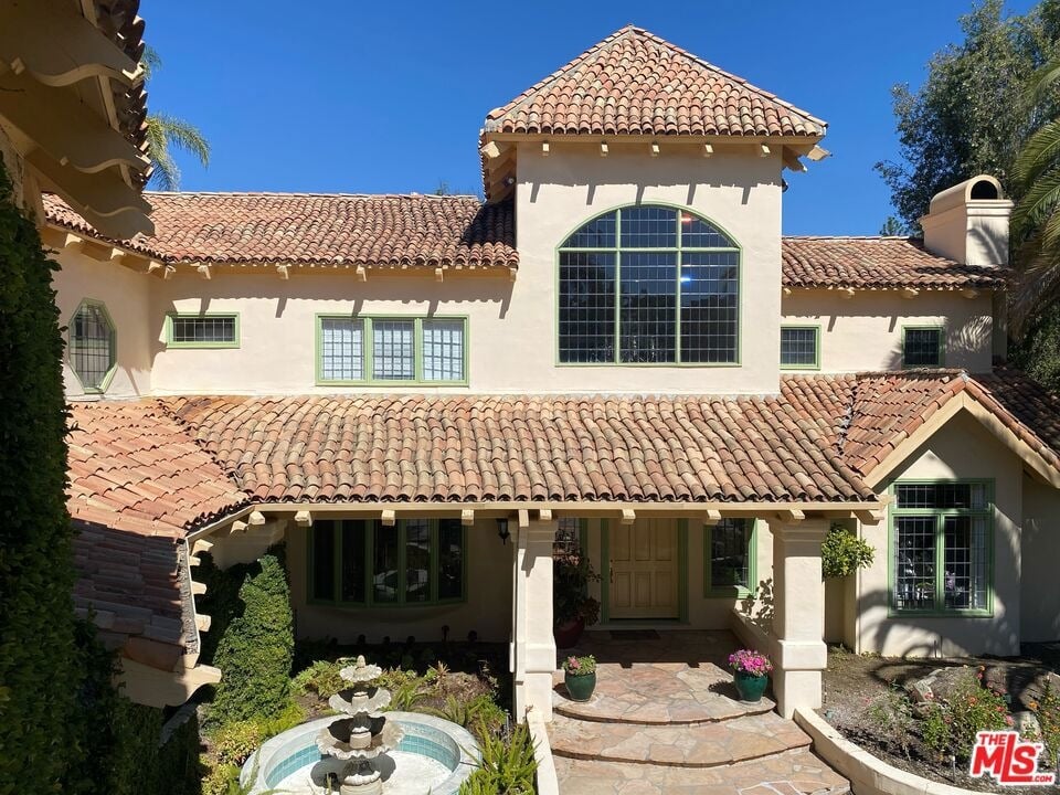 Two-story stucco home with a clay tile roof, arched window, and courtyard fountain.