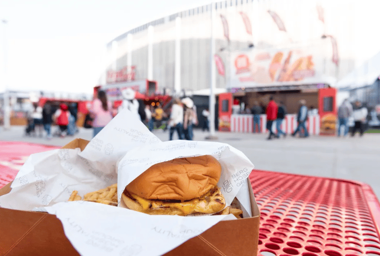 Cheeseburger in branded paper on a red table at an outdoor rodeo food stall.