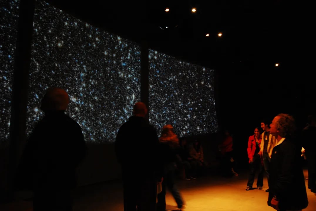 Visitors look at a star field projected onto a large wall inside the Morrison Planetarium.