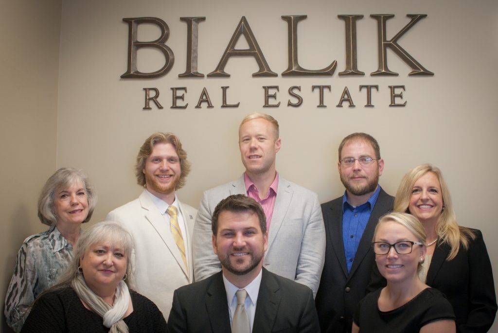 Eight Bialik Real Estate agents pose beneath the company sign.