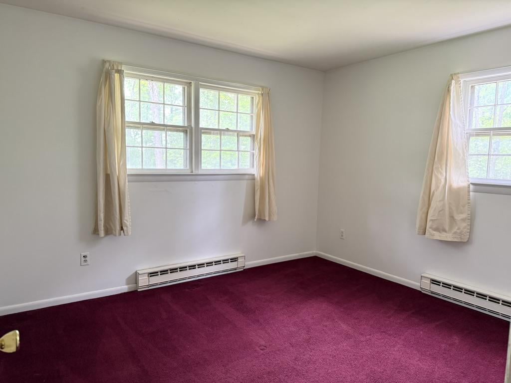 Empty bedroom with burgundy carpet, cream curtains, and three windows.