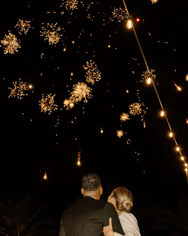 A couple watching fireworks light up the night sky under string lights on Pioneer Day in Utah
