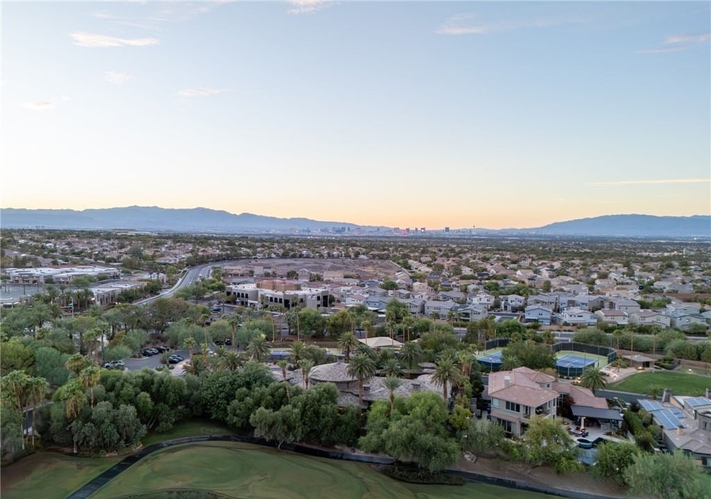Drone view from above a MacDonald Highlands fairway across Henderson to the Las Vegas Strip skyline and Spring Mountains at dusk