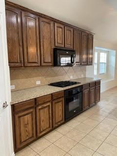 Kitchen with dark wood cabinetry, built-in microwave, black cooktop and oven, and beige tile flooring.
