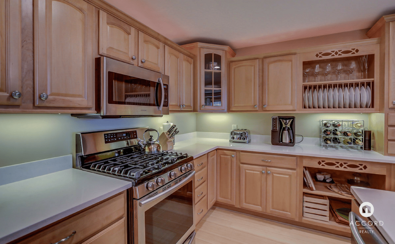 Condo kitchen with honey-colored cabinets, white countertops, and stainless steel appliances.