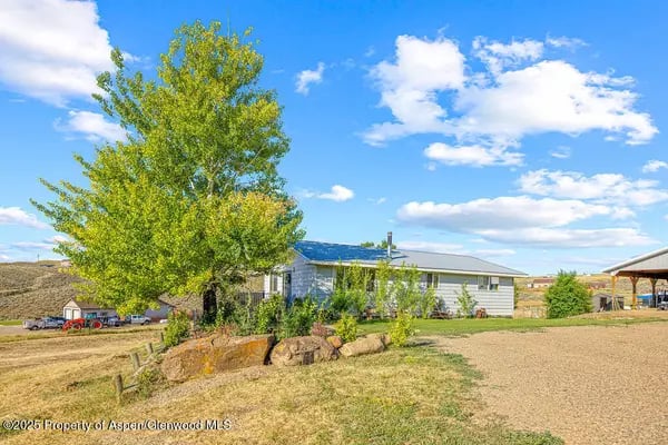 Single-story Craig home with solar panels, a large leafy tree, and boulders in the yard.