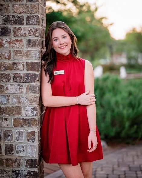 Anna Rogers in a red sleeveless dress beside a brick column.