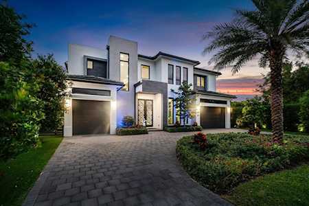 Modern two-story home with a paved driveway, twin garages, and a palm tree at dusk.