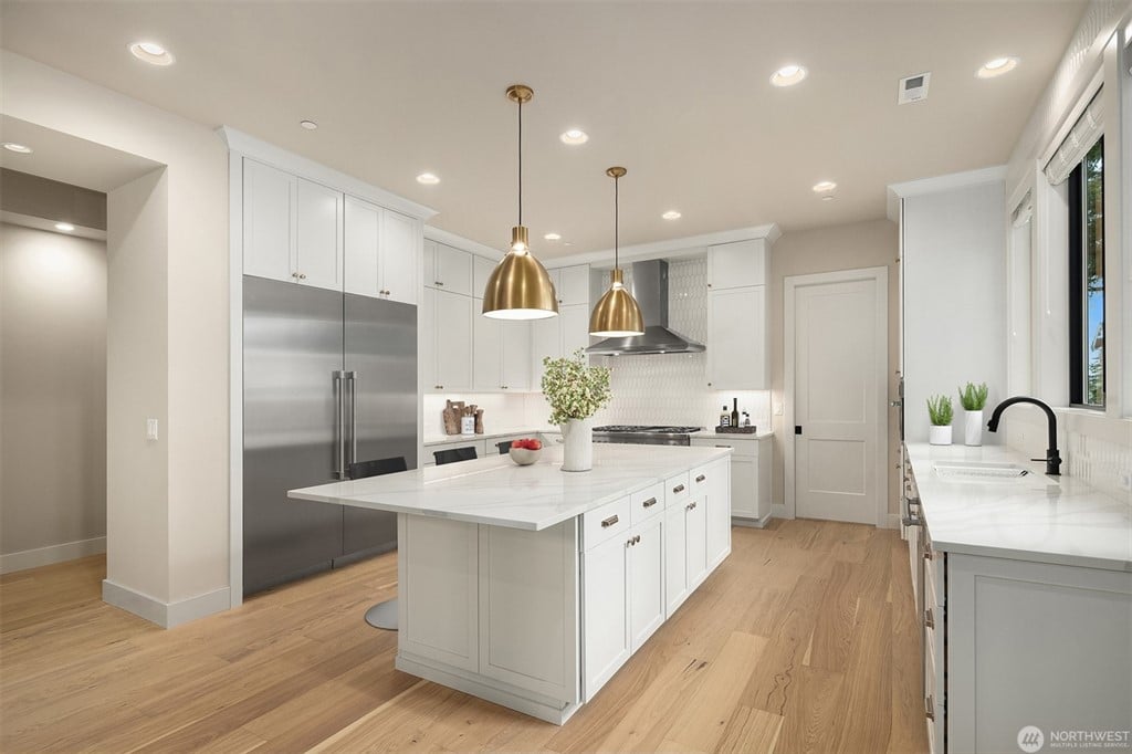 uxury modern kitchen with white cabinetry, quartz countertops, stainless steel refrigerator, gold pendant lighting, and hardwood floors, ideal feature in upscale homes.