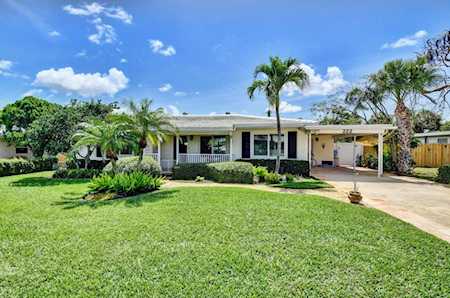 Single-story home with a covered porch, attached carport, broad lawn, and palm landscaping.