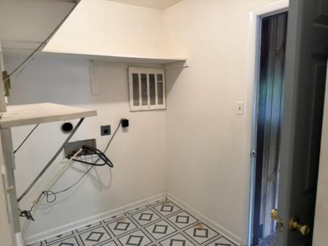 Vacant utility room with built-in shelves, exposed wiring, and geometric tile flooring.