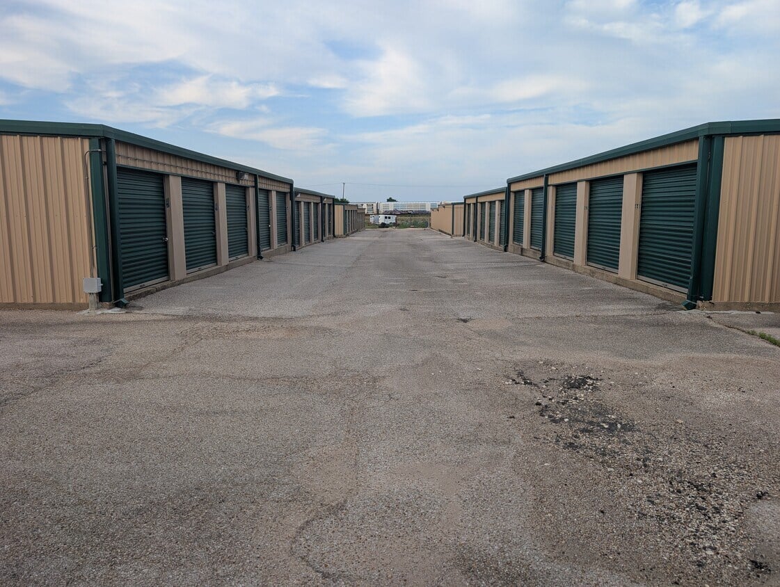 Self-storage units line a wide paved drive beneath a partly cloudy sky.