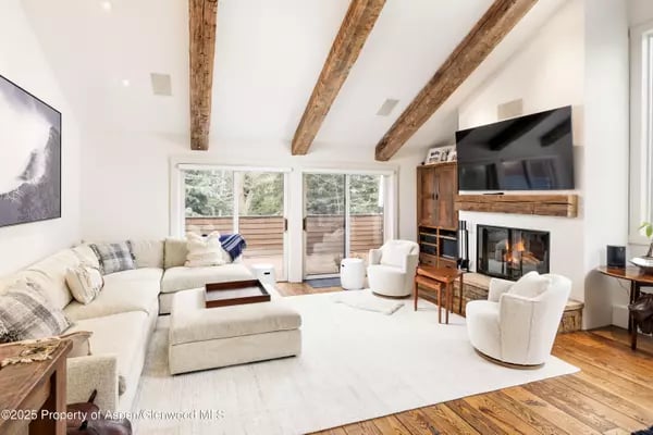Living room with exposed wood beams, a pale sectional sofa, sliding doors, and a fireplace.