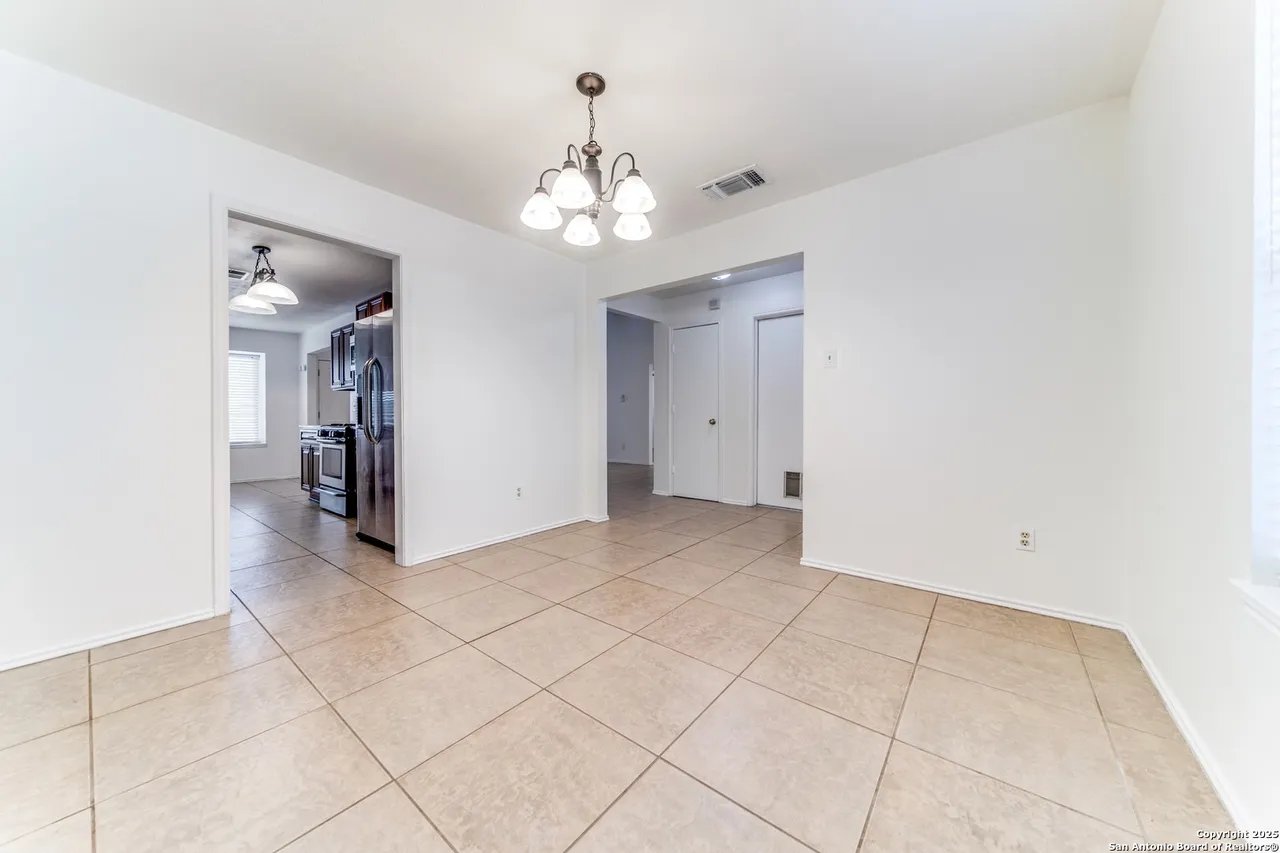 Empty tiled dining area with a chandelier and an opening into the kitchen.